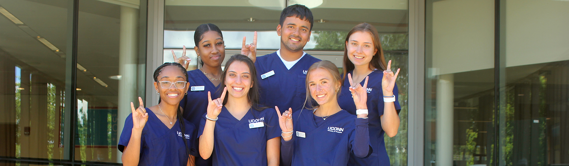 Transitions to clinical group 8 A group of six students wearing blue scrubs making Husky sign