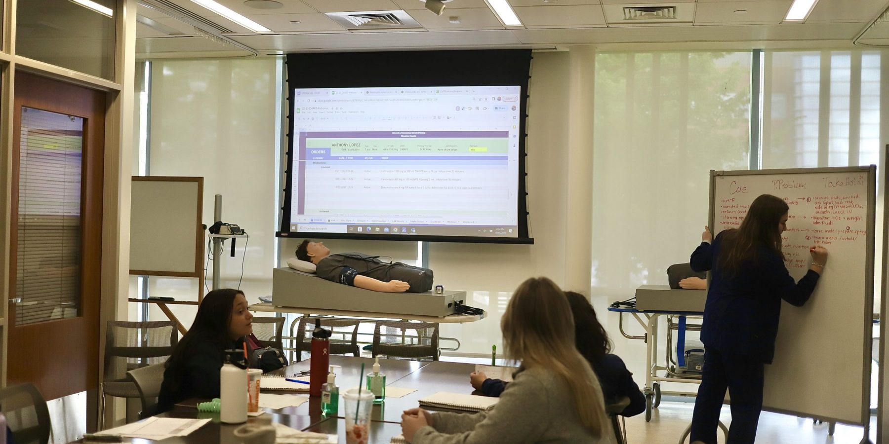 sim lab learning Student writing on whiteboard in front of sim lab and three students watching